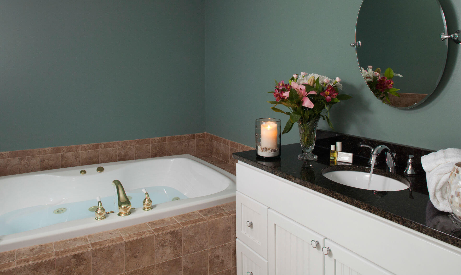 Jetted spa tub next to sink with flowers and candle