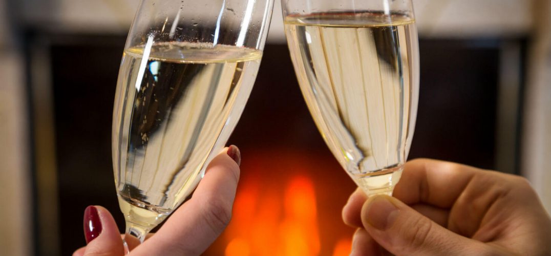 Two people toasting with champagne glasses in front of fireplace