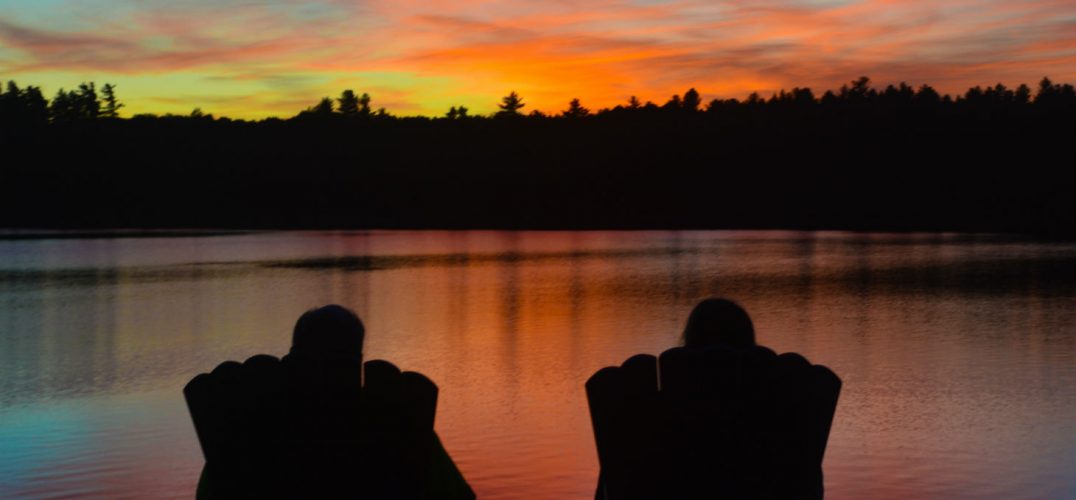 Silhouette of couple watching sunset together across lake