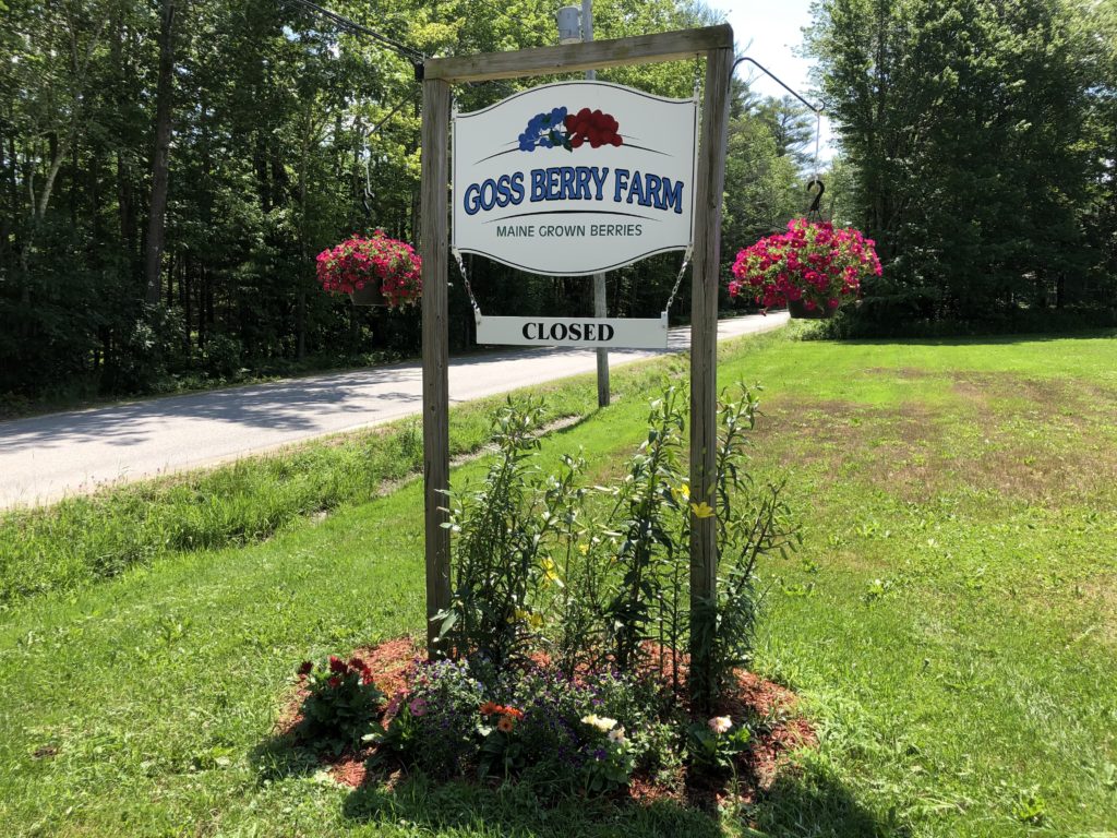 Goss Berry Farm sign surrounded by green grass and hanging baskets of flowers