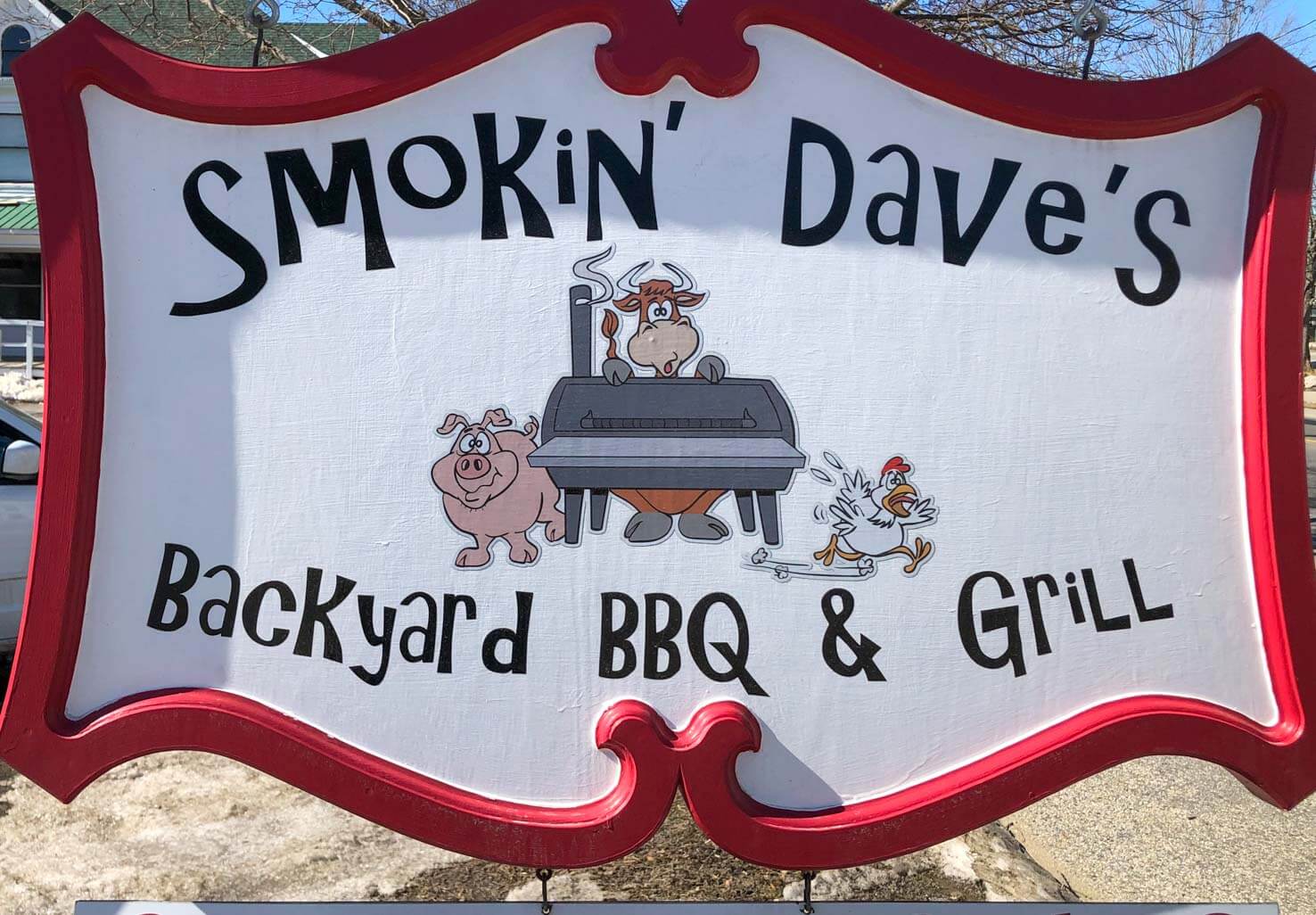 Sign for Smokin' Dave's with cartoon cow, pig and chicken by a BBQ grill