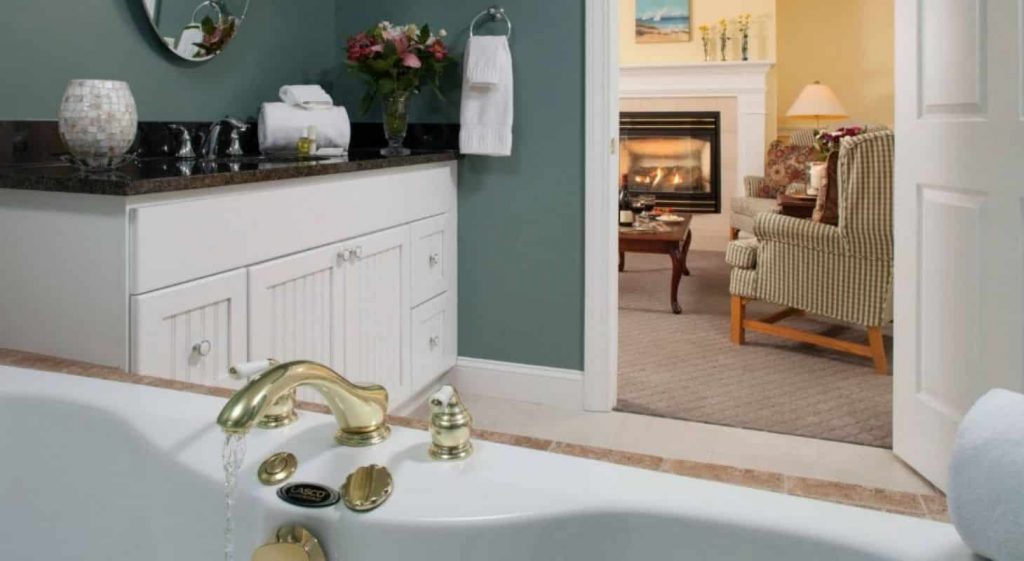 Guest bath with light blue walls, soaker tub, and view of cozy fireplace through the doorway to the guest room