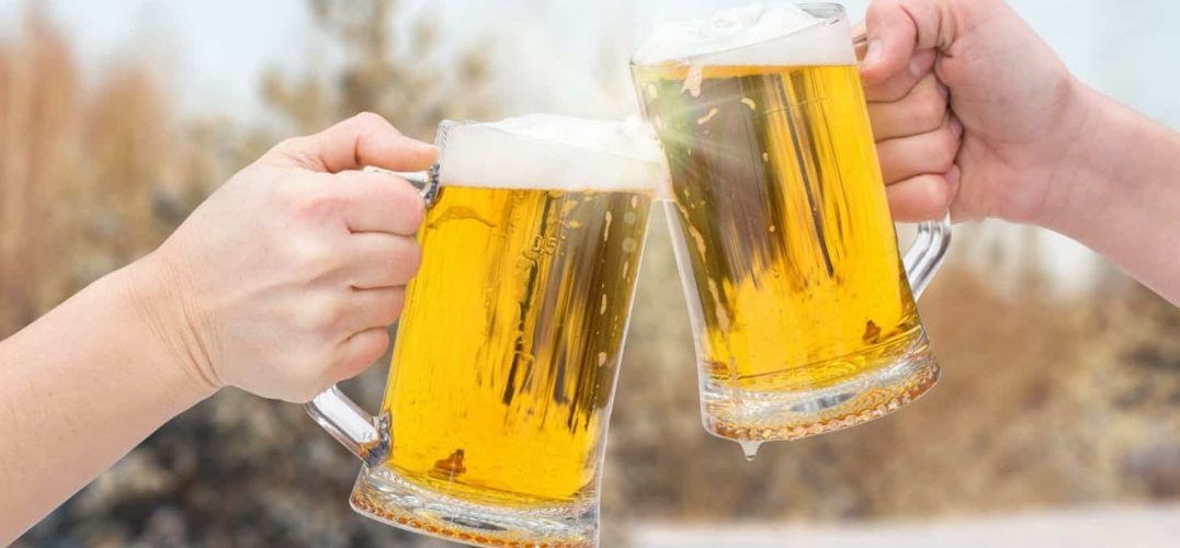 Two people's hands clinging beer mugs outdoors in the winter
