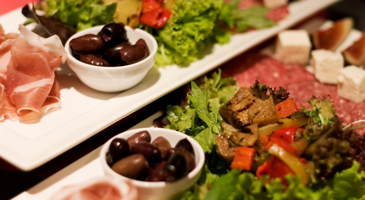 Two white ceramic platters topped with proscuitto, olives, cheese