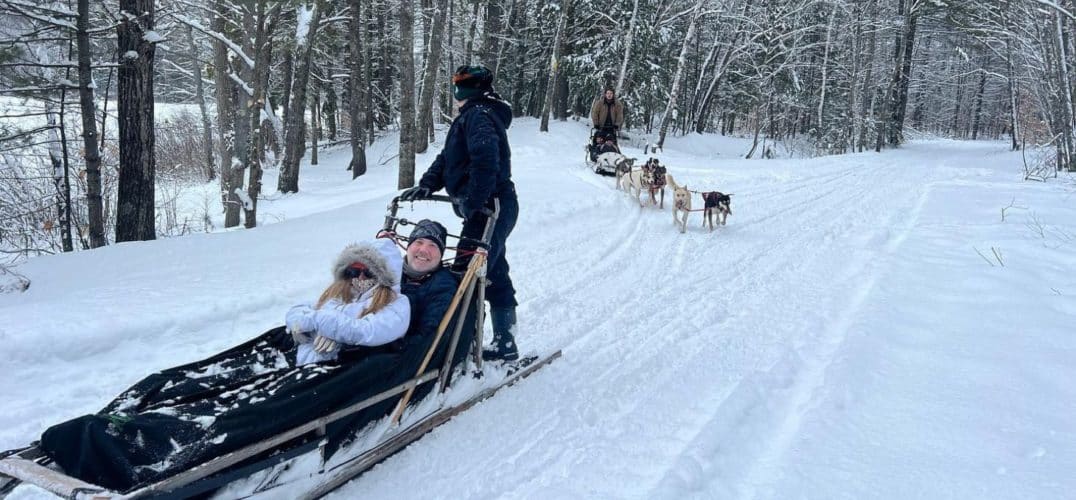 Husky and guide-led dog sleds pulling couples through the snowy woods.