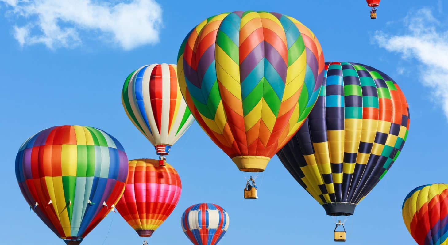 Brightly colored hot air balloons floating in a blue sky with wispy white clouds