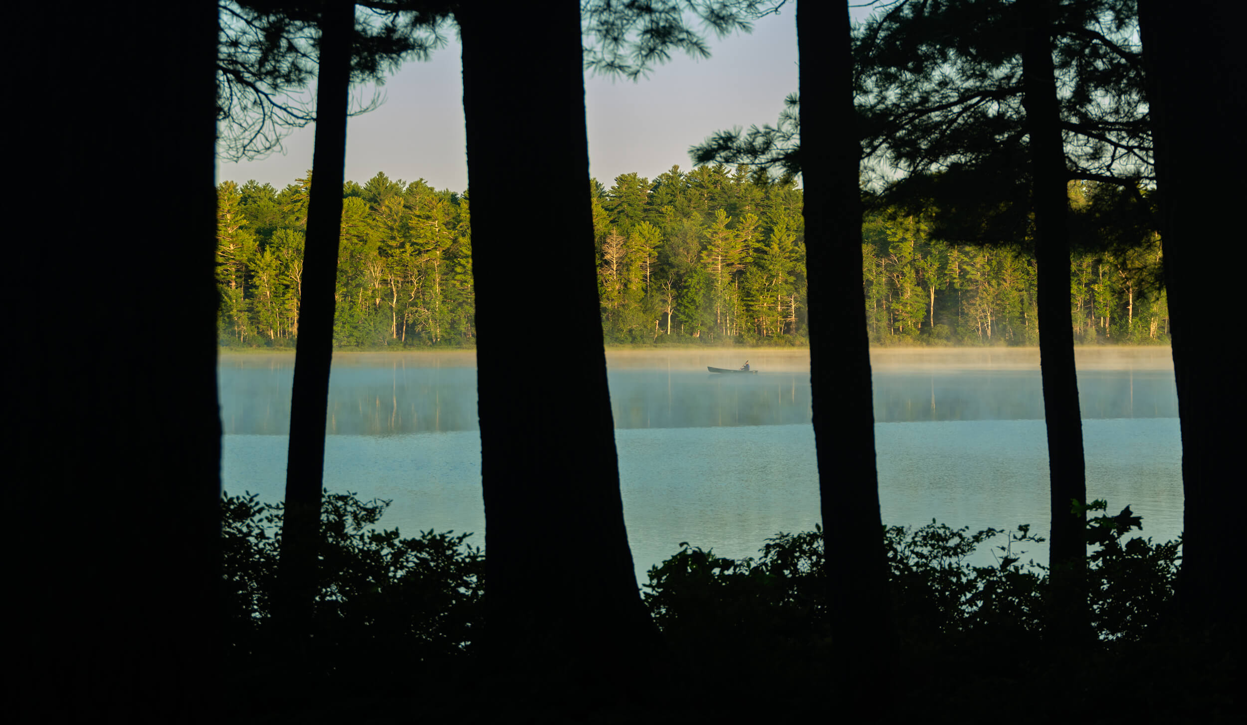 A guest takes out a canoe on Tripp Lake at sunrise 