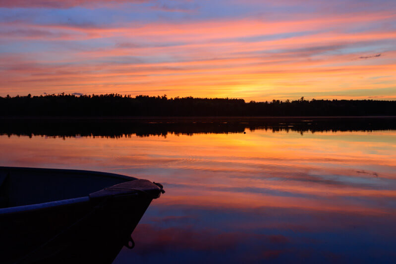 sunset with blues, purples, oranges and yellow reflecting on lake with boat in foreground